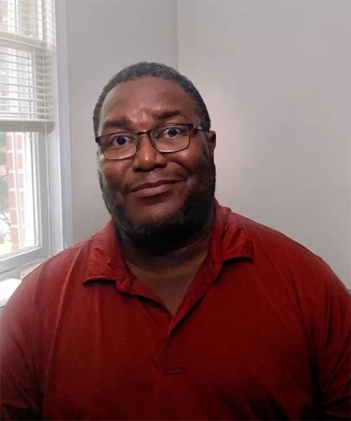 Richard sitting and facing the camera with a soft smile
